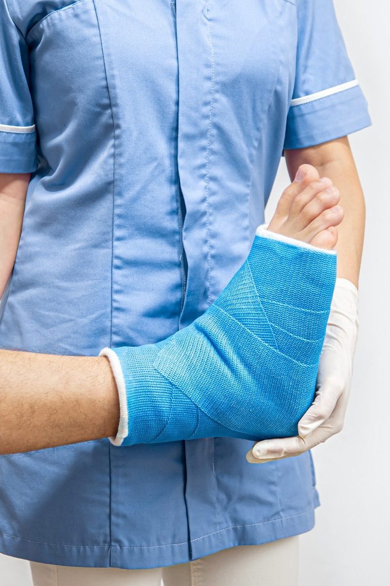 Female doctor in a blue medical gown checking broken leg on male patient.
